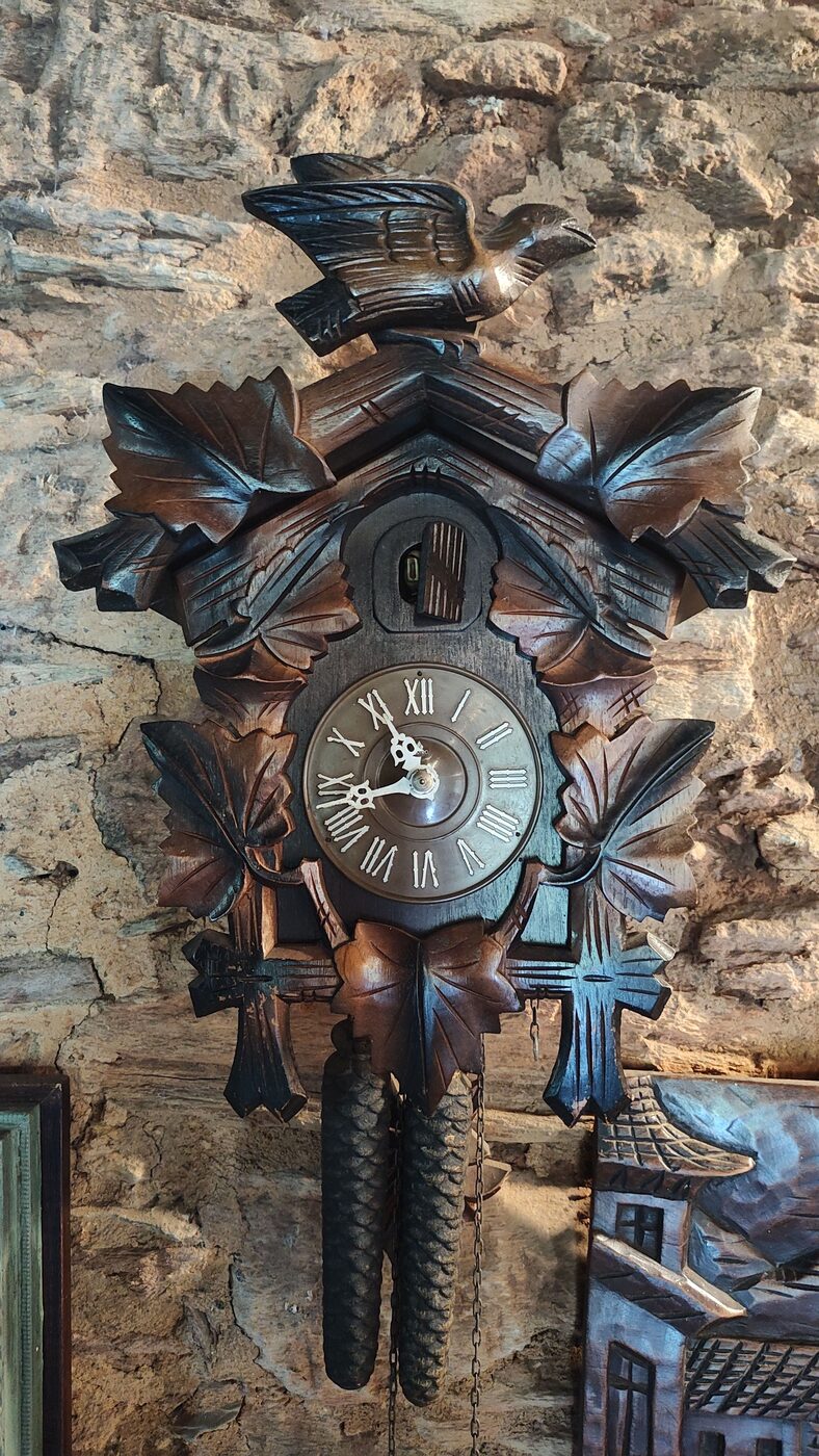 Carved Black Forest cuckoo clock with bird crest, leaf carving, Roman-numeral dial and pinecone weights